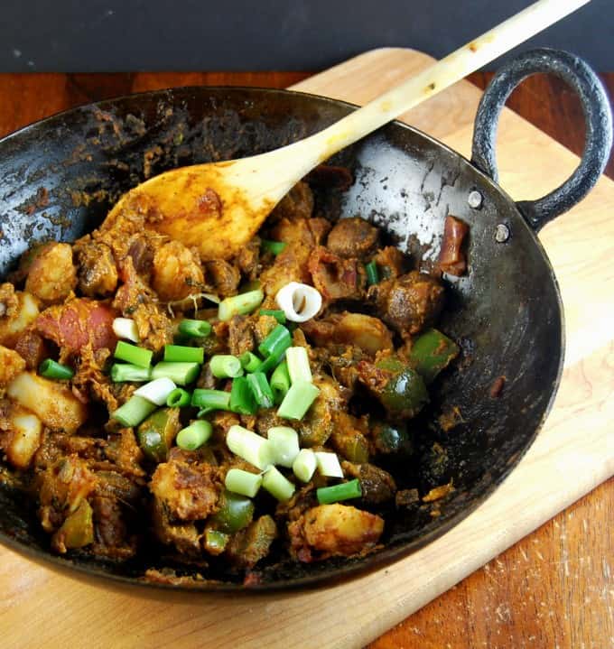 Vegetable Balti in a cast iron wok or karahi with a wooden spoon.