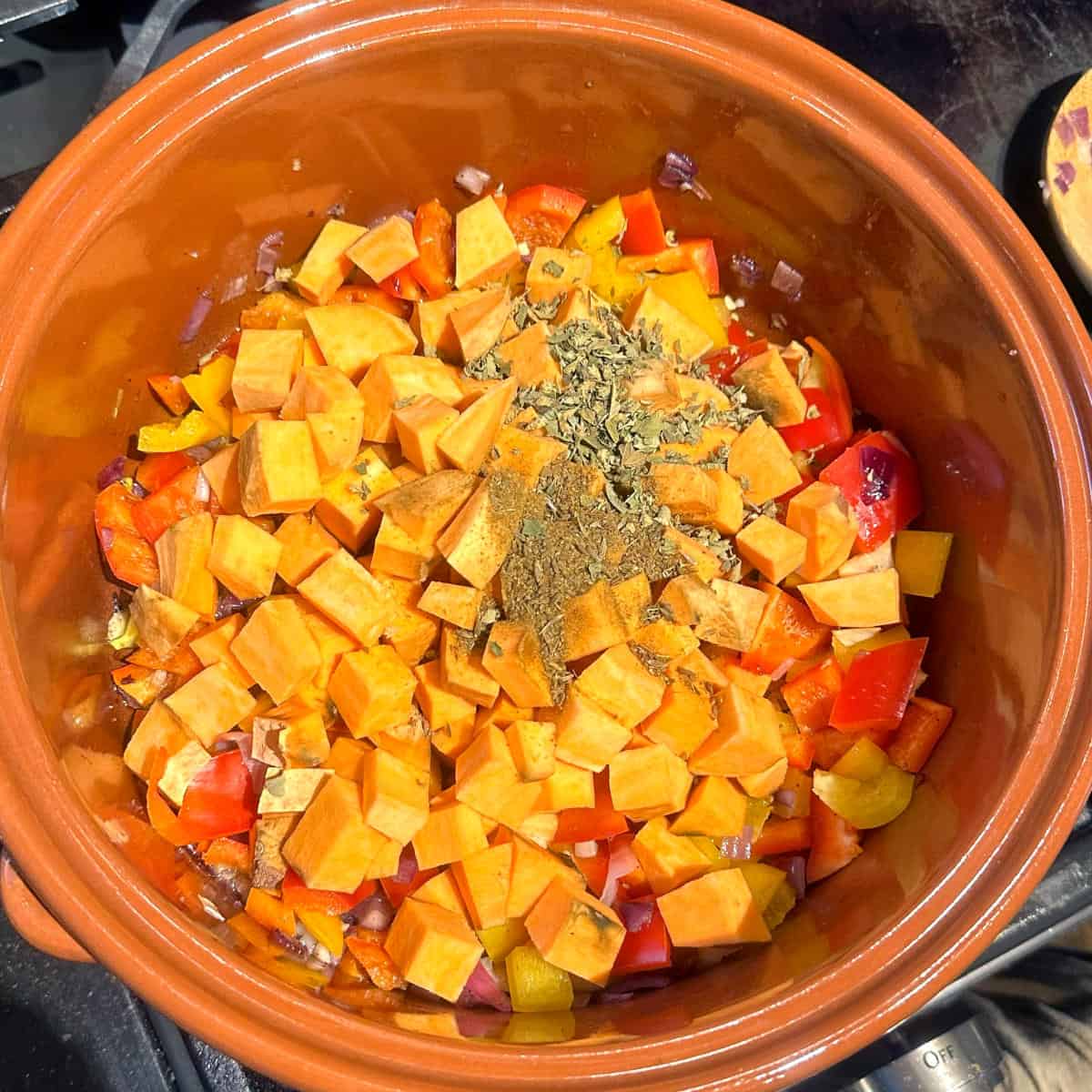 Sweet potatoes and herbs and spices added to pot with bell peppers and onions.