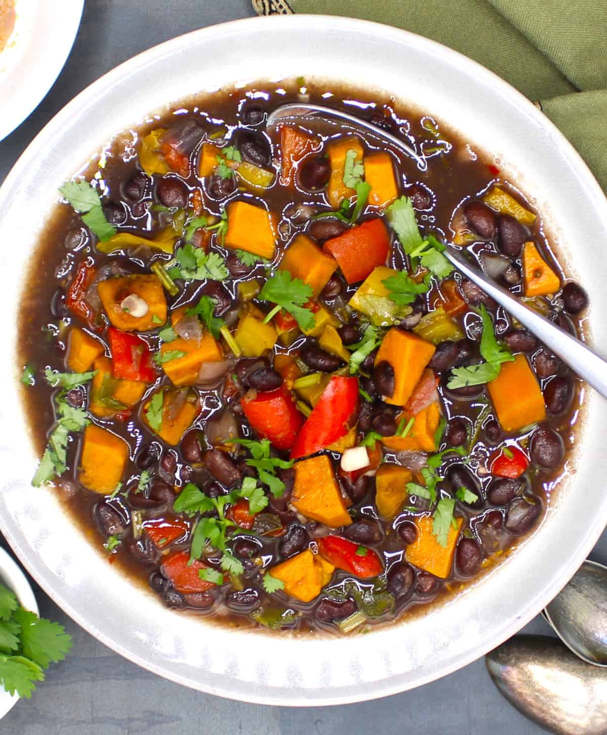 Cuban black beans with colorful bell peppers, sweet potatoes and cilantro in bowl with spoon.