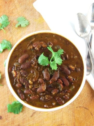 Rajma, Indian kidney beans in a tomato onion sauce, in a white ceramic bowl with a cilantro garnish. Next to it is a white napkin on a wood background