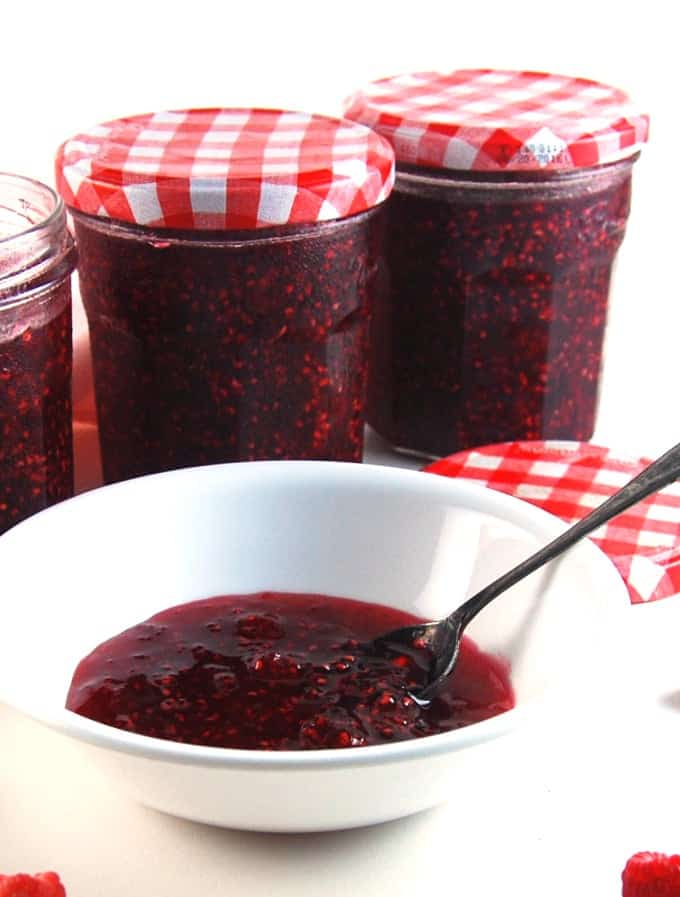Homemade raspberry jam in white bowl with jars of jam in the background.