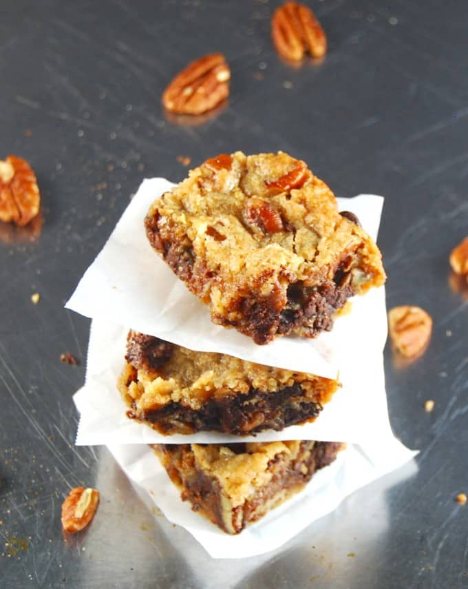 Vegan chocolate chunk bars stacked on a baking sheet with parchment paper between them and pecans scattered around.