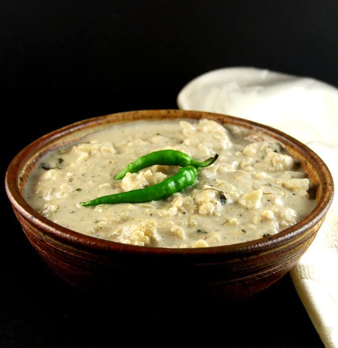 Creamy malai gobi curry in an earthen glazed bowl with green chili peppers on top.