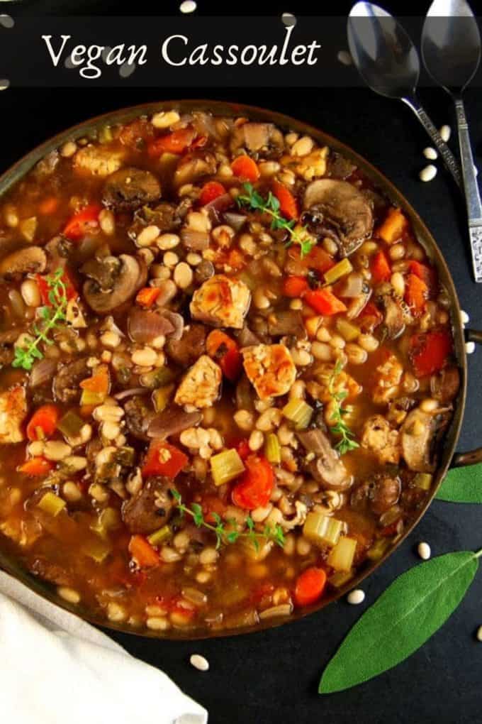 Vegan Cassoulet in a copper pan with white beans and sage leaves scattered around