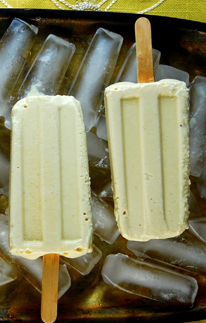 Vegan pineapple cheesecake popsicles on ice on silver tray.