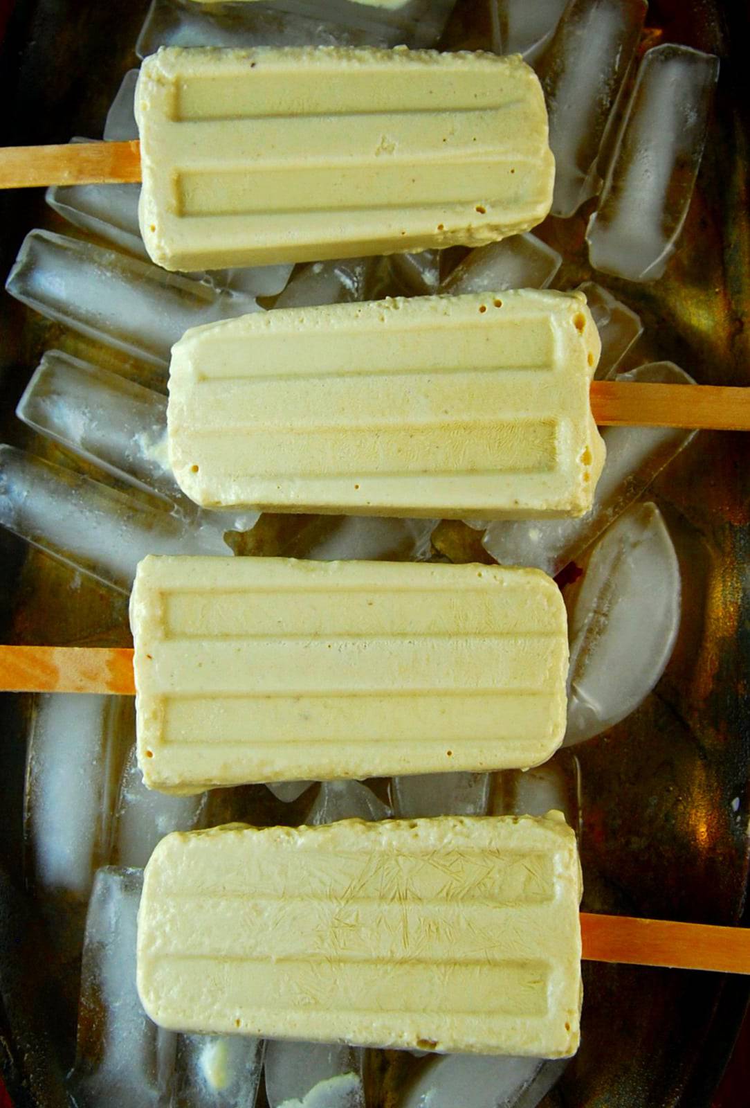 Pineapple cheesecake popsicles on ice in silver tray.