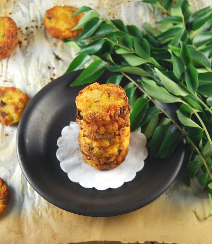 Baked, fat-free potato vadas on black plate with curry leaves.