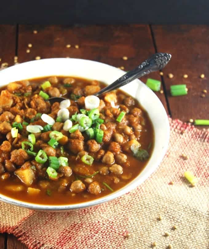 Slow Cooker Chana Masala in a white bowl with scallions and a spoon on a wood table.