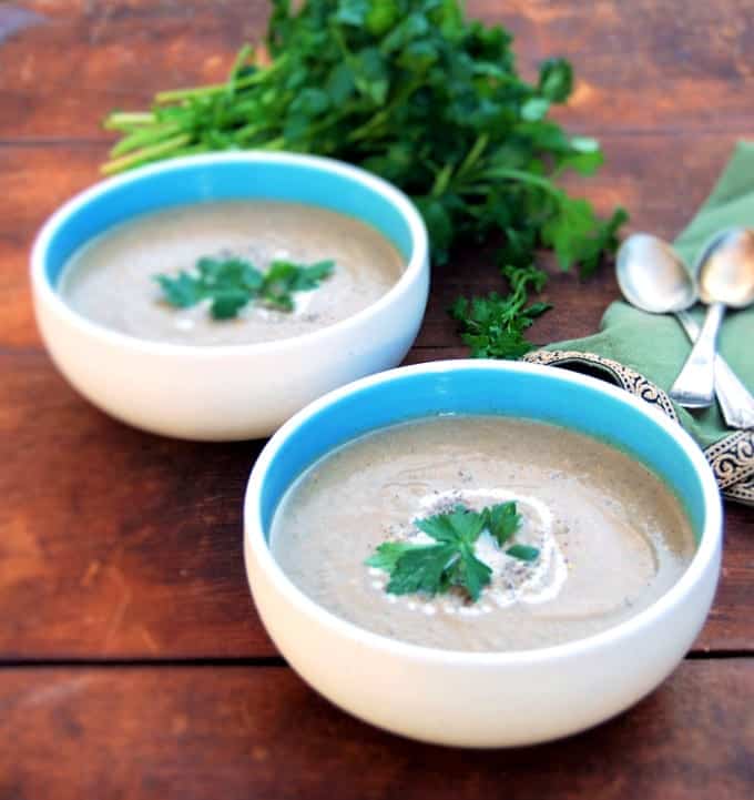Photo of Smoky Roasted Eggplant Soup with Za'atar served in two blue and white bowls with parsley and two spoons with a green napkin in the background.