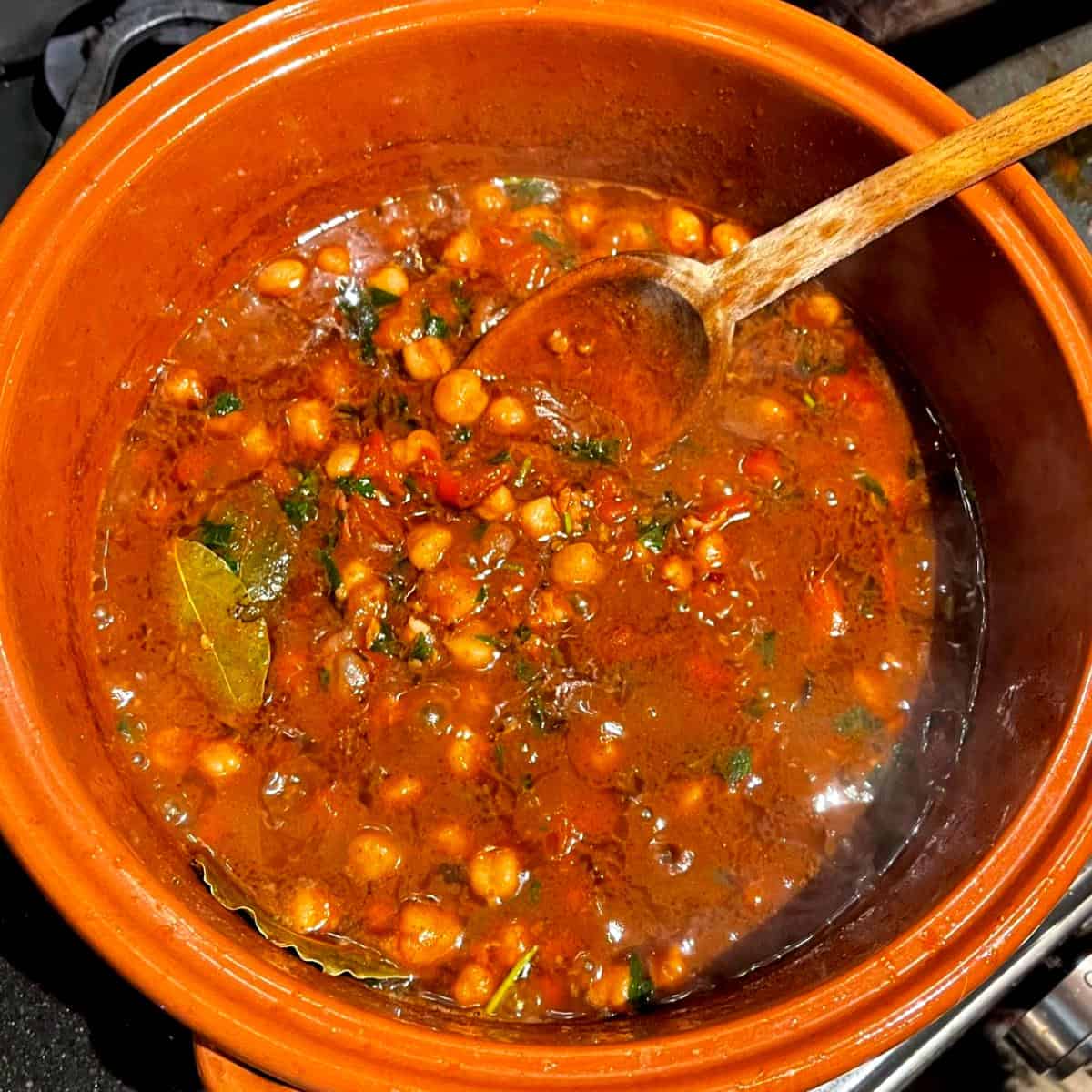 Parsley added to cooked Lebanese chickpea stew in clay pot.
