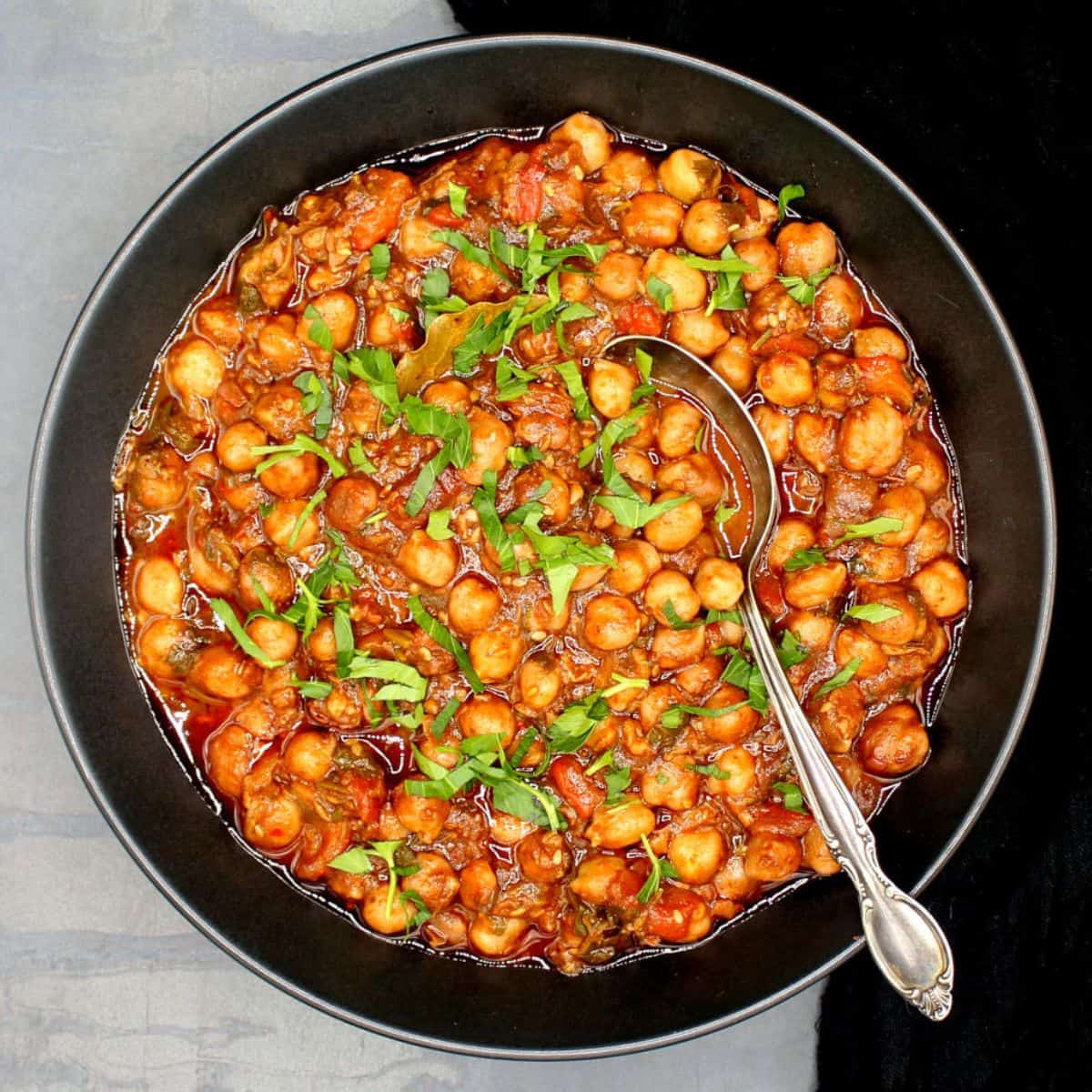 Lebanese chickpea stew in black bowl with spoon.