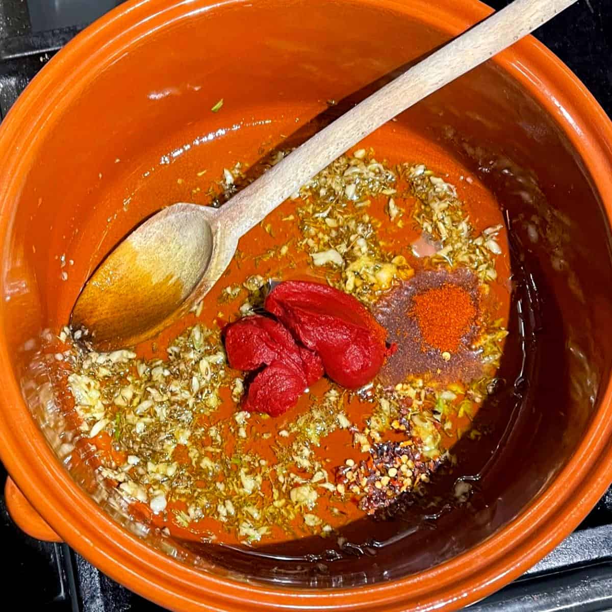 Tomato paste, paprika and red pepper flakes added to pot with garlic and cumin.