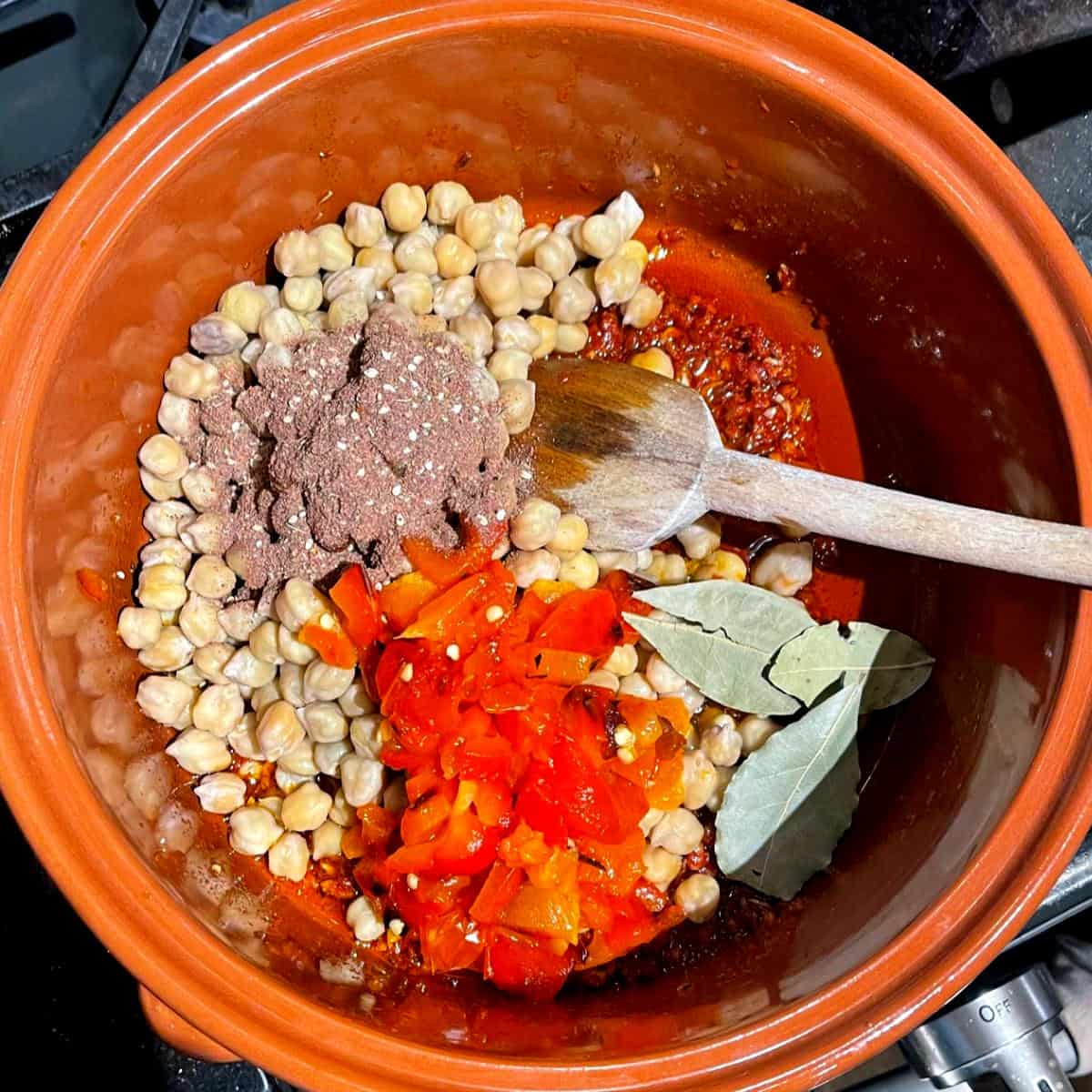 Za'atar, bay leaves and red peppers added to chickpeas and spices in clay pot.