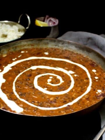 Front partial shot of vegan dal makhni or dahl makhani with a swirl of cashew cream and rice in background