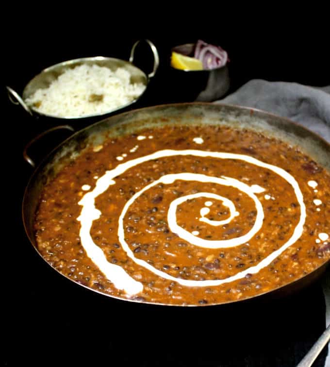 Vegan dal makhani or dahl makhani in a copper serving dish with cashew cream, jeera rice, lemons and onion