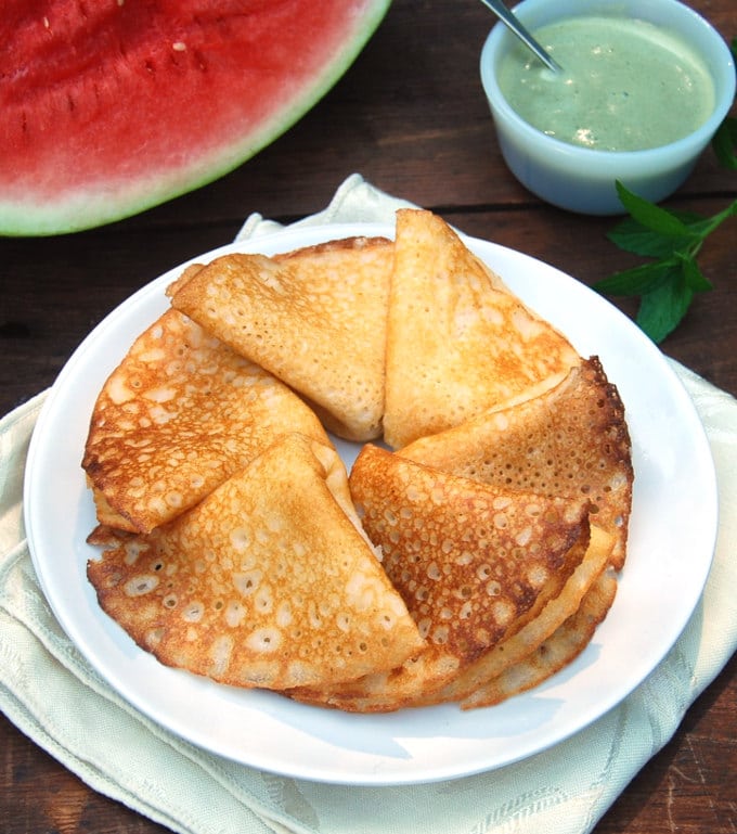 Watermelon Rind Dosa folded in white plate with watermelon slice and chutney in background.
