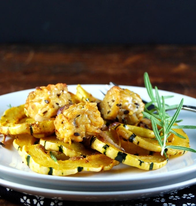 Roasted delicata squash with tempeh, onions and curry spices and a sprig of rosemary in white plate.