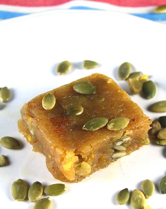 One vegan Chana Dal Burfi, a vegan Indian sweet, on a white plate with pumpkin seeds.