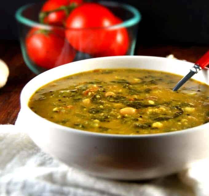 Garlicky Spinach Dal in white bowl with tomatoes in background.