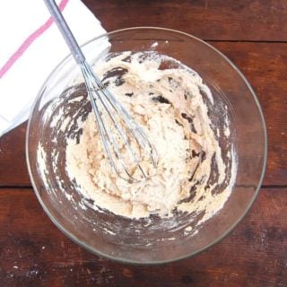 Sourdough starter made with flour and water in a bowl with a whisk and a kitchen napkin