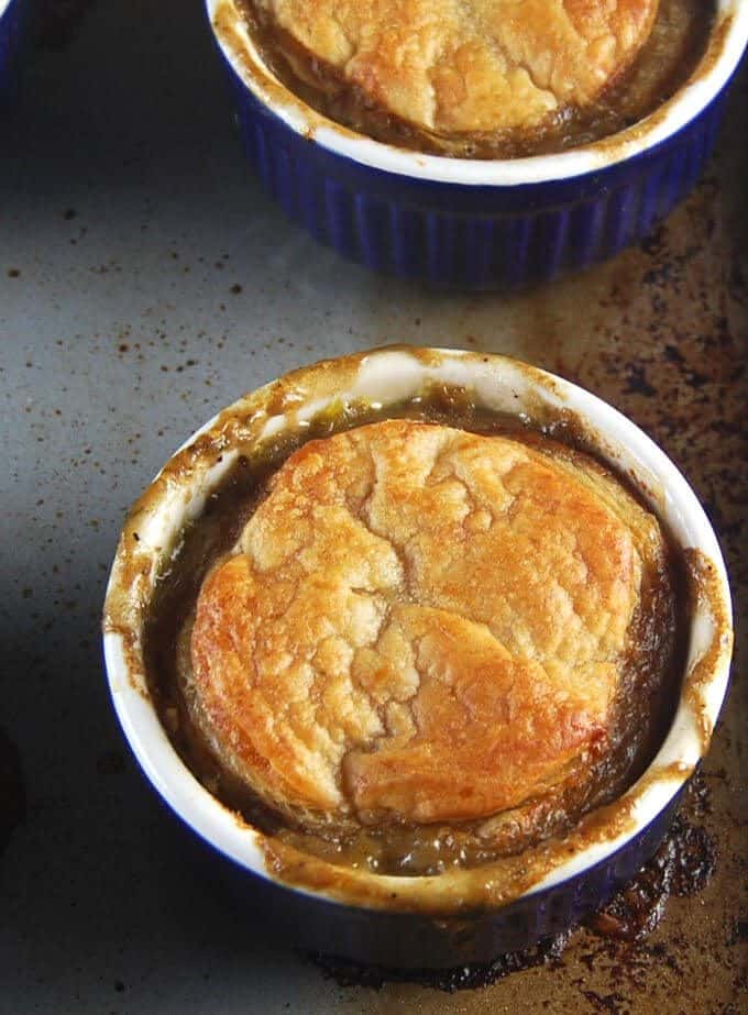 Overhead shot of a mushroom pot pie with golden puff pastry crust in a blue and white ramekin with one more ramekin in the background, all on a baking sheet.