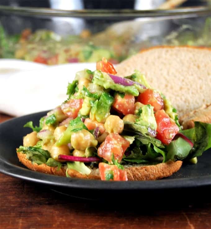 Vegan chickpea avocado salad for wraps and sandwiches in black plate on bread.