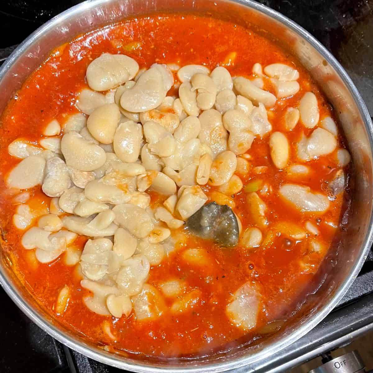 Lima beans added to tomatoes in saucepan.