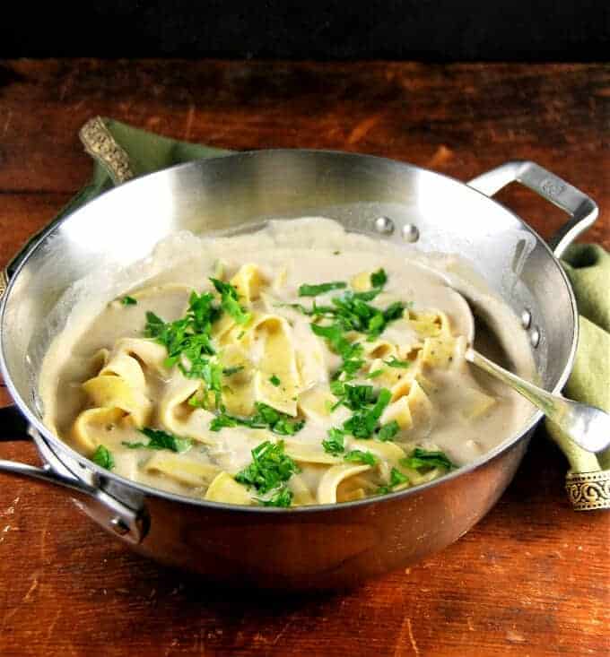 Photo of vegan white pasta sauce in steel saucepan with a broad ribbon pasta and parsley.