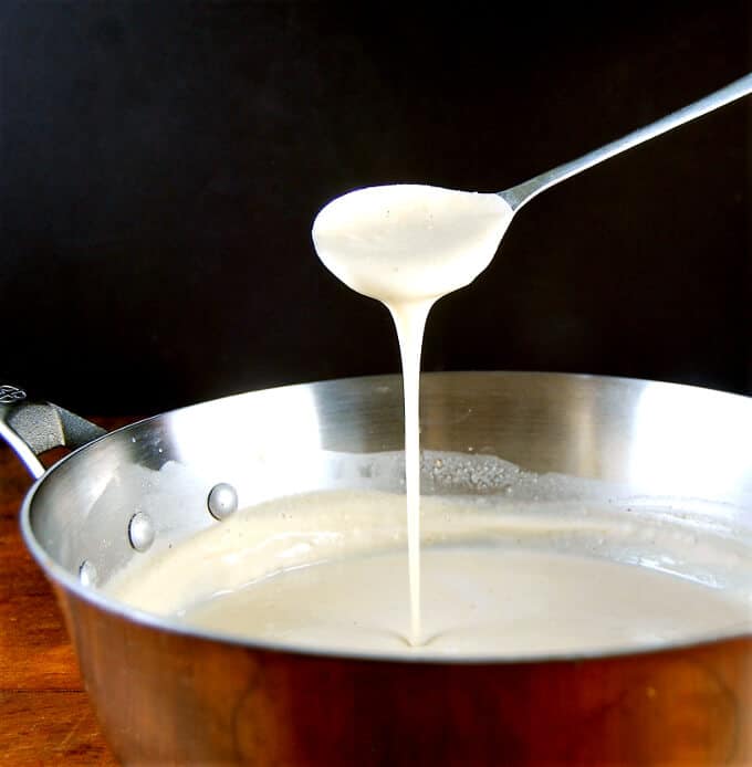 Photo of the best vegan white pasta sauce being poured into a saucepan with a spoon.