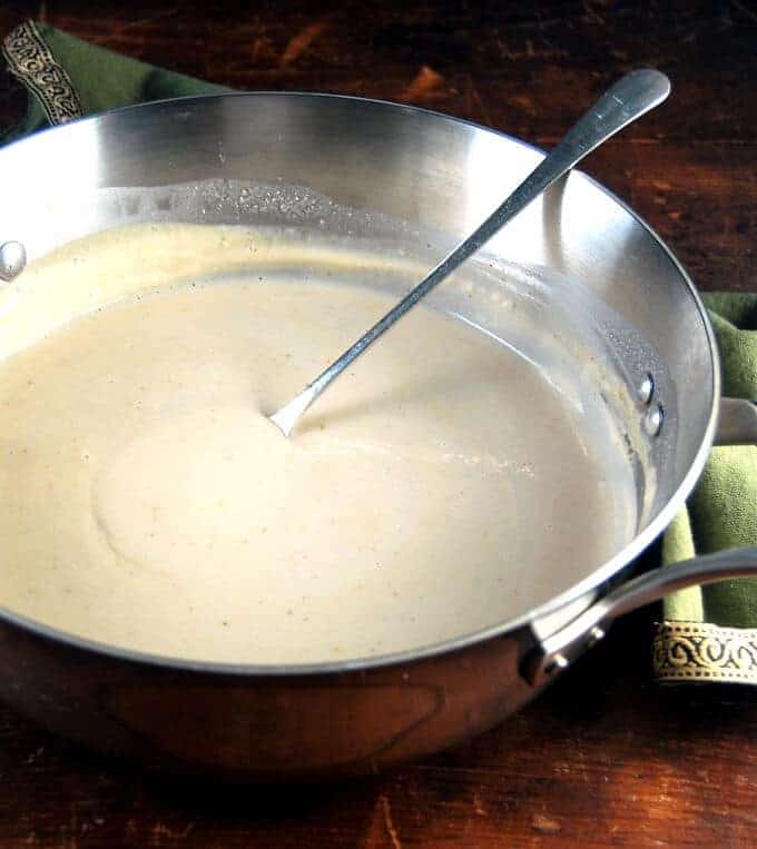 Photo of the best vegan white pasta sauce in a saucepan with a spoon.