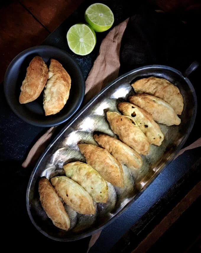 Chickpea and Kale Stuffed Empanadas on silver tray and two empanadas on a black plate.