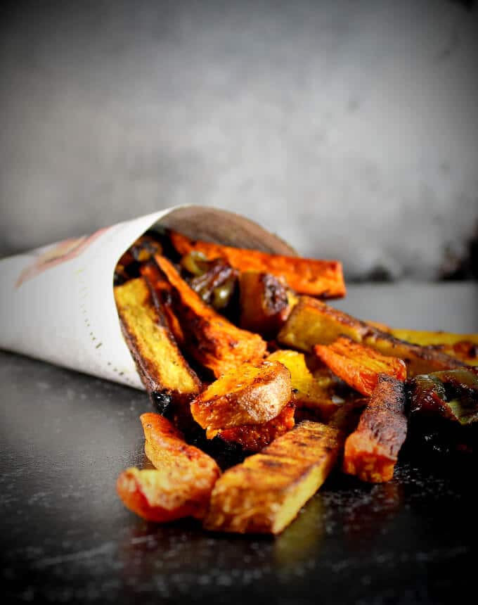 Turmeric Roasted Root Vegetables in a paper cone spilling onto a slate countertop.