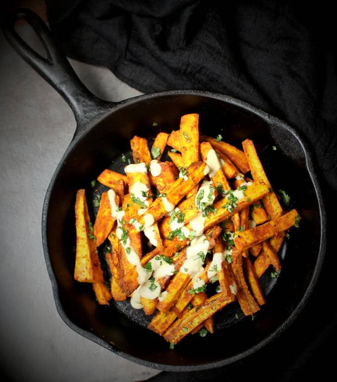 Baked plantain fries in skillet drizzled with cheezy sauce and cilantro.