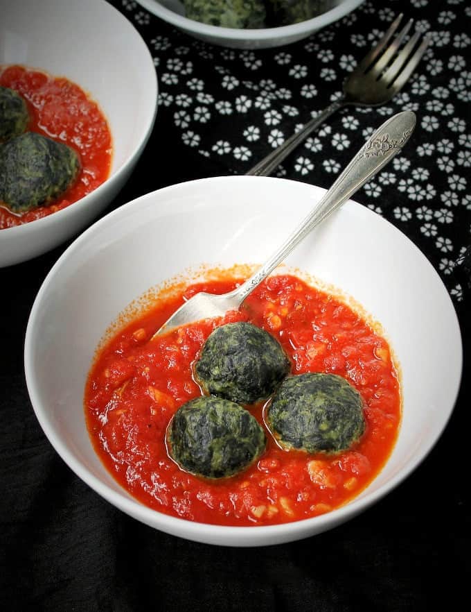 Spinach Cashew Ricotta Dumplings in a Marinara Sauce served in a white bowl with a silver fork.