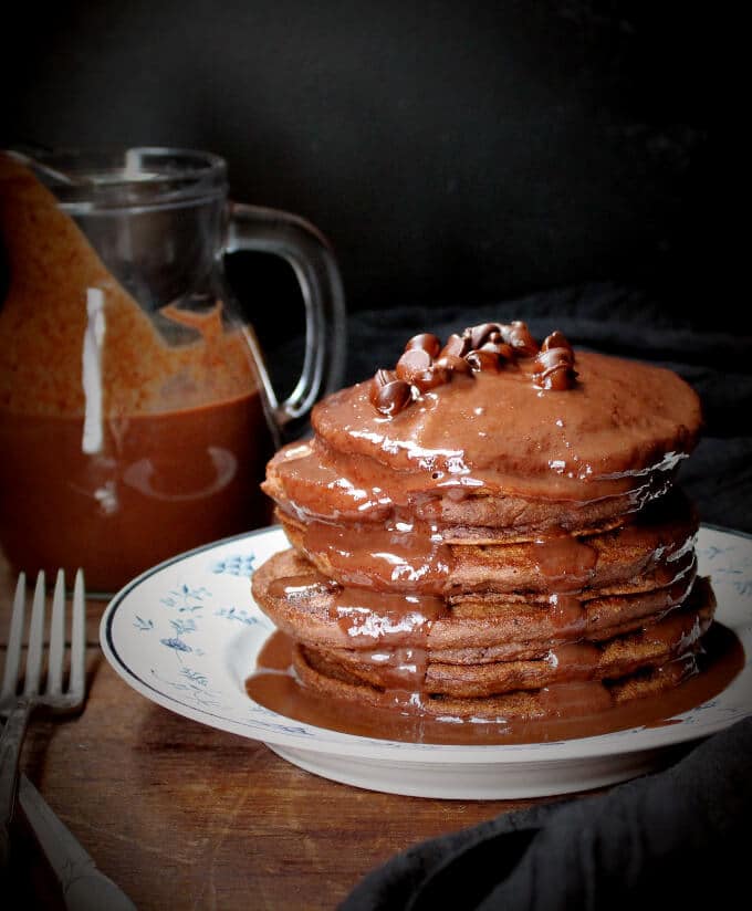 Photo of vegan double chocolate pancakes with chocolate sauce poured all over and chocolate chips.
