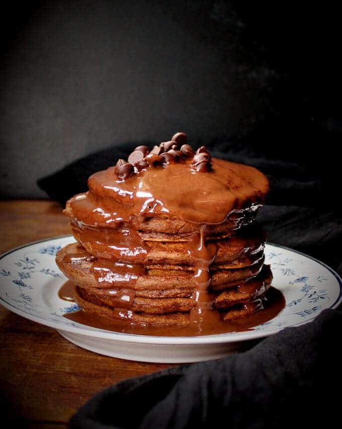 Vegan Double Chocolate Pancakes with chocolate chips and chocolate sauce stacked in a blue and white plate.
