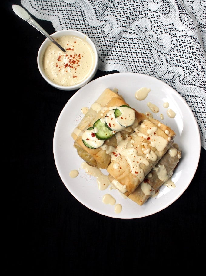 Overhead shot of Vegan baked chimichangas with filo and lentil stuffing in a white plate with cucumber slices and magic cheese sauce.