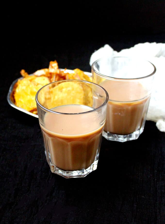 Vegan Cutting Chai served in two ribbed tumblers with a plate of bhujia or pakoras.