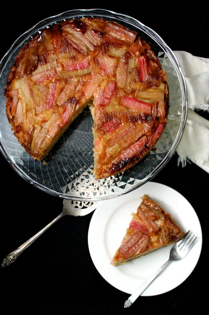 Overhead photo of a slice of vegan rhubarb ginger upside down cake with a soft, moist crumb and a mosaic-like top of glossy pink rhubarb stalks on a glass cake stand.