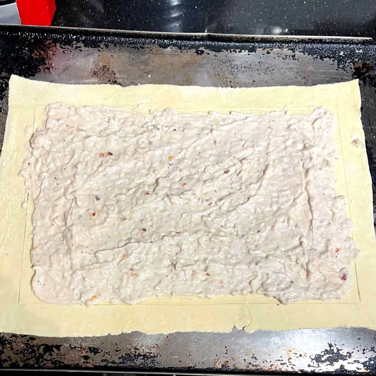 Crust rolled out and layered with vegan bechamel sauce for asparagus pizza.
