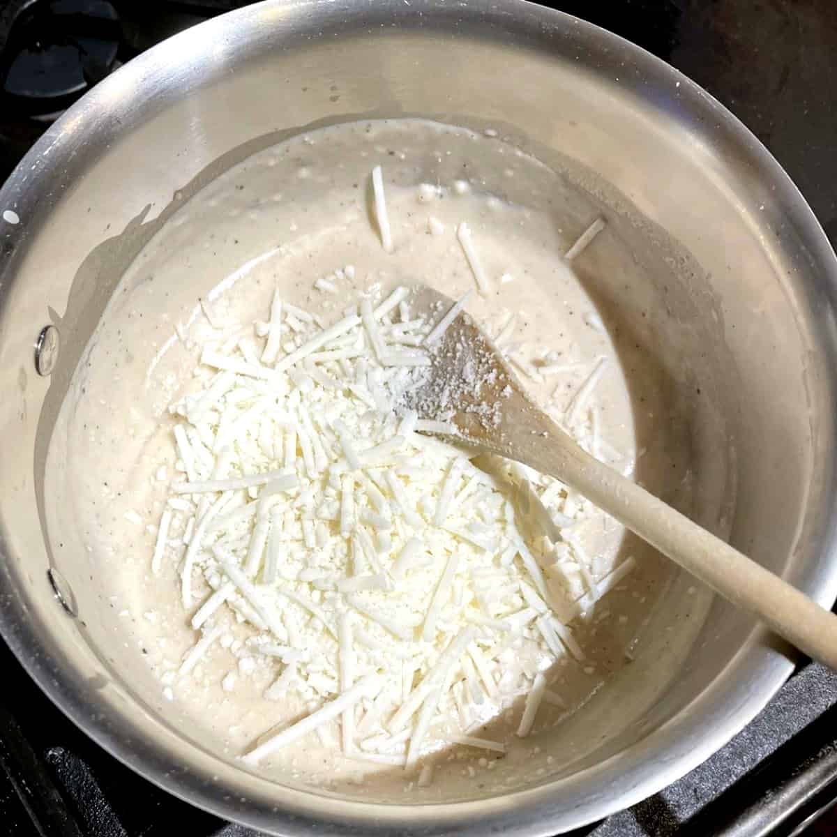 Vegan cheese added to bechamel sauce in saucepan.