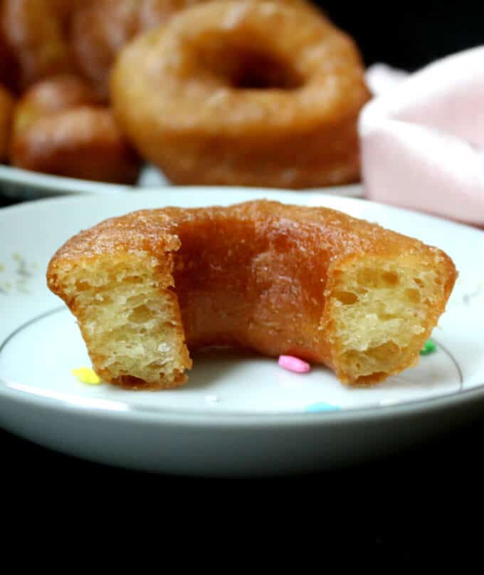 A cross section of a vegan brioche donut, light and airy, on a white plate with star-shaped sprinkles and a pink napkin. More donuts in background.
