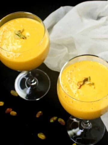 Vegan mango lassi in two glasses with nuts scattered around and as a garnish.