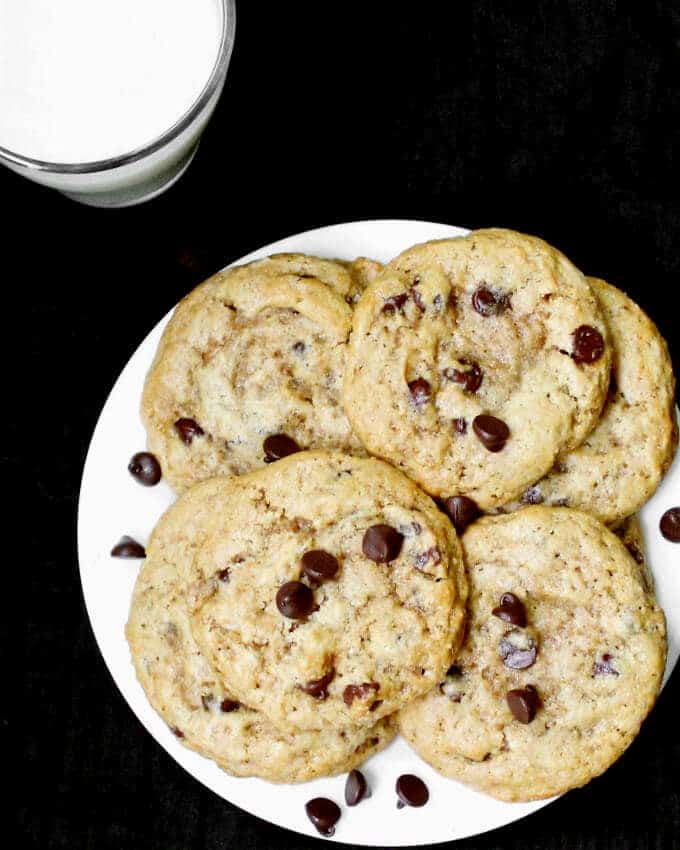 A white plate with vegan chocolate chip cookies and a glass of milk beside it
