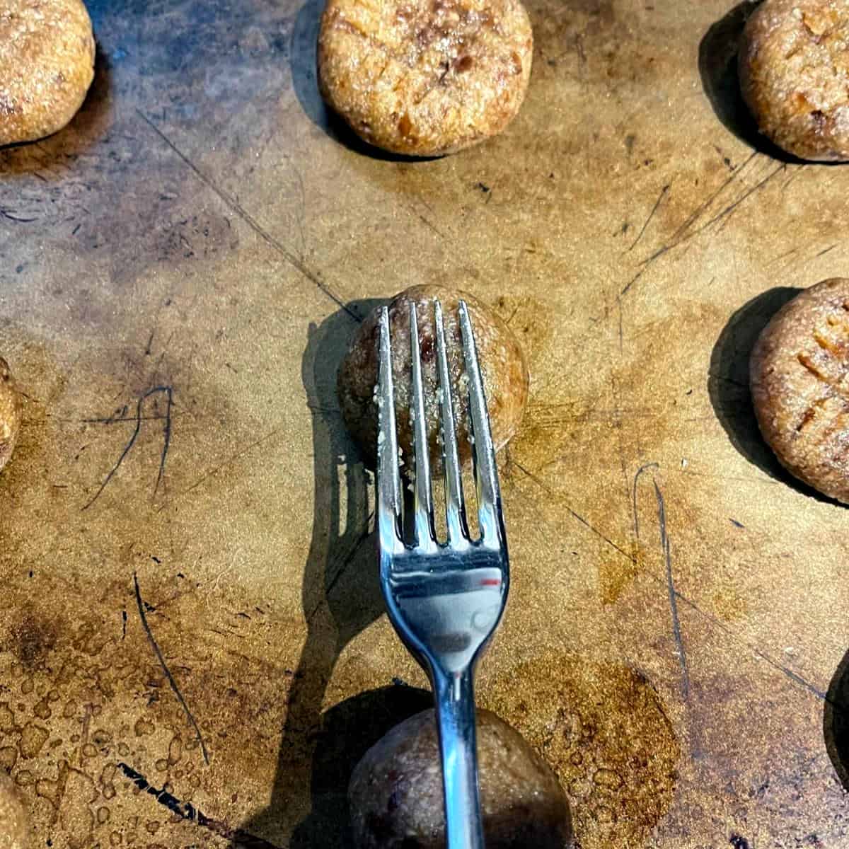 Pressing on cookie dough balls with tines of fork.