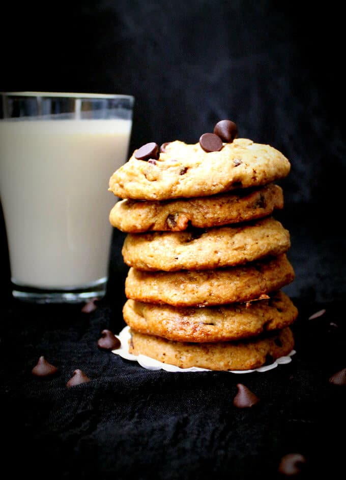 Chewy vegan chocolate chip cookies stacked with a glass of milk next to them.