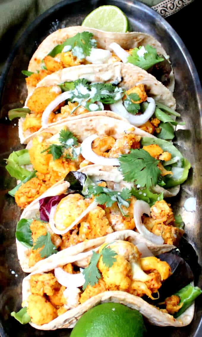Overhead closeup of Cauliflower Tempeh Masala Tacos with onions, cilantro and greens.