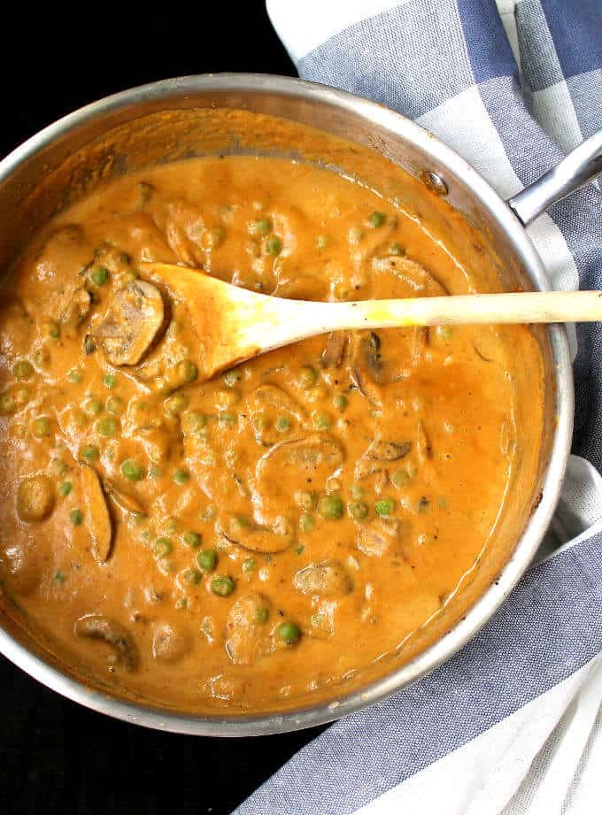 Photo of mushroom matar, a mushroom and peas curry with a thick gravy, in a saucepan with a wood ladle and blue and white napkin.