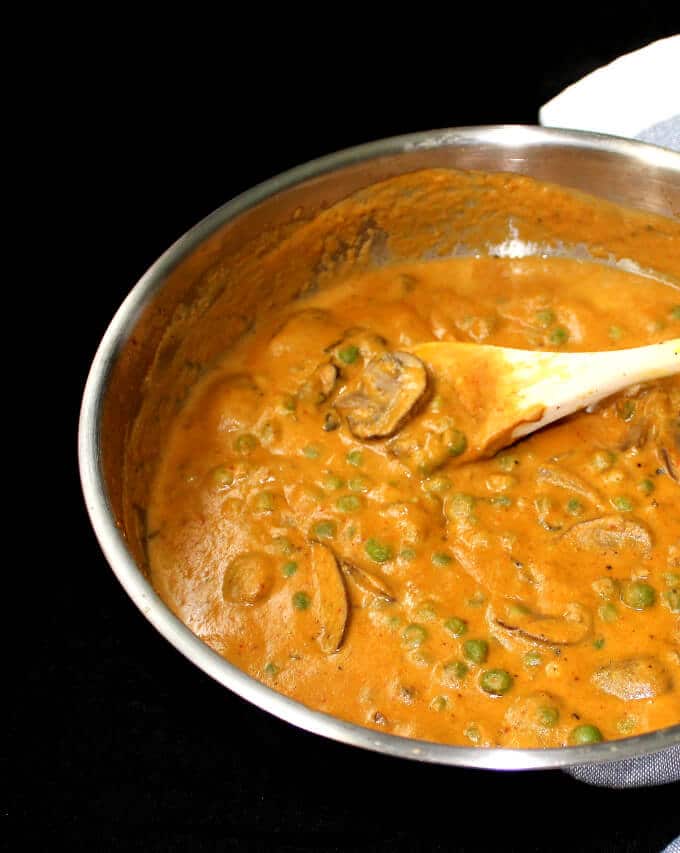 Photo of mushroom matar, a mushroom and peas curry with a thick gravy, in a steel saucepan with a wooden ladle.