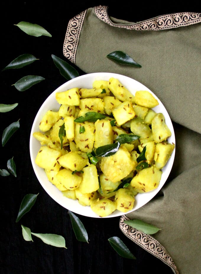 Overhead shot of a bowl of jeera aloo or cumin potatoes with curry leaves.